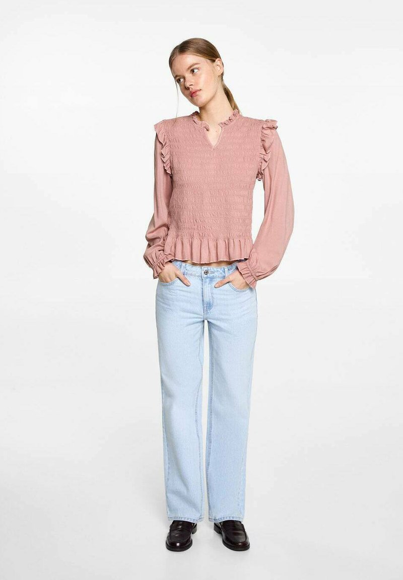Dammig rosa smockad topp med volanger på axlarna, V-ringning och utsvängd nederkant. Matchas med ljusblå raka jeans och svarta skor.