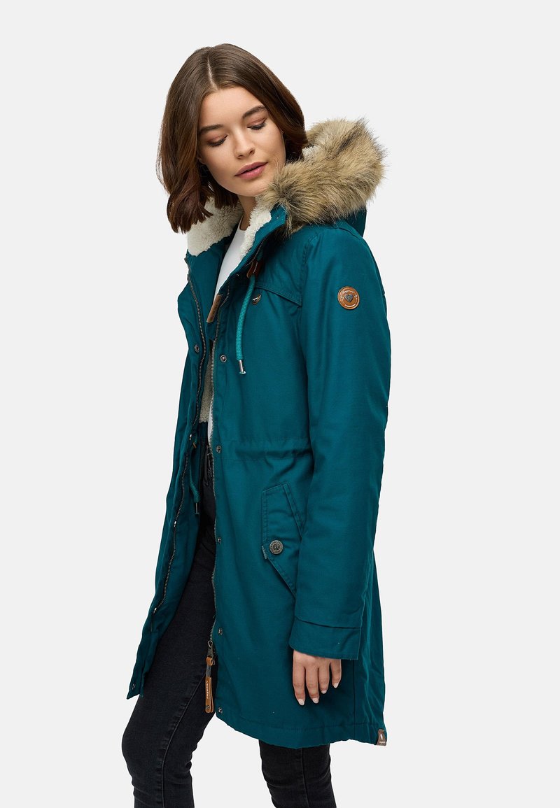 Parka teal con cappuccio bordato in pelliccia, chiusura con zip e bottoni, due tasche laterali e patch con logo sul petto. Tessuto testurizzato con finitura liscia.