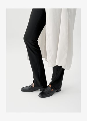 Crne kožne mokasine s četvrtastim vrhom i niskom blok petom, uparene s crnim uskim hlačama i lepršavim bijelim vanjskim slojem.