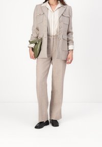 Blazer en tweed gris clair avec boutons dorés et double poche plaquée, assorti à un pantalon taille haute. Chemise rayée blanche et beige en dessous.