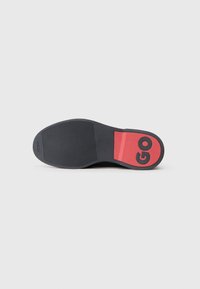 Crna gumena potplat cipele s crvenim naglaskom i oznakom "GO" otisnutom na peti. Tekstura grip uzorak za bolju prionljivost. Glatka površina u cjelini.