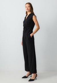 Zwart gestreepte jumpsuit met een getailleerde top, V-hals en wijde broekspijpen. Gladde stof met een subtiele glans en zijzakken.