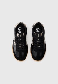 Baskets noires avec des accents à motif serpent, dotées d'une empeigne texturée, d'une pointe arrondie et de lacets noirs. Semelle en caoutchouc avec une légère bande de roulement.