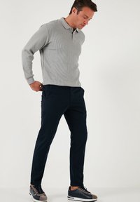 Grijze longsleeve poloshirt met geribbelde textuur, gecombineerd met donkerblauwe broek en grijze sport schoenen met blauwe en witte accenten.