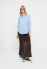 Chemise bleu clair à boutons avec manches longues, associée à une jupe longue plissée foncée et des baskets noires. Design clair et minimaliste.