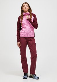 Giacca aderente bicolore con parte anteriore trapuntata rosa e maniche color marsala; abbinata a pantaloni marsala coordinati e calzature con motivo e accenti blu.