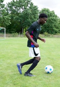 Black Nike jersey with pink and blue accents, white shorts, black socks, and blue soccer cleats, dribbling a blue and white soccer ball on grass.