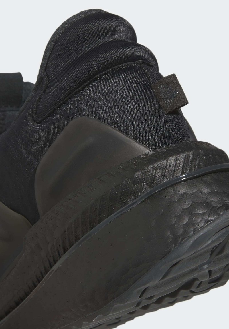 Schwarzer Sportschuh mit einer strukturierten Oberfläche und gepolstertem Kragen. Verfügt über eine gummierte Sohle mit Muster und einem flexiblen Design für Unterstützung.