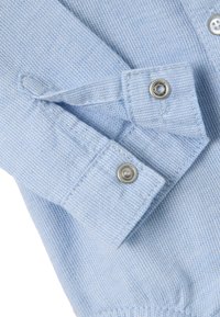 Camisa abotonada azul claro con tejido texturizado, puño con botón a presión plateado y sutiles rayas diagonales.