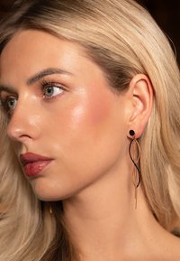 Black and gold earrings with elongated, intertwining shapes and a round black stud at the top, suspended with thin metallic strands.