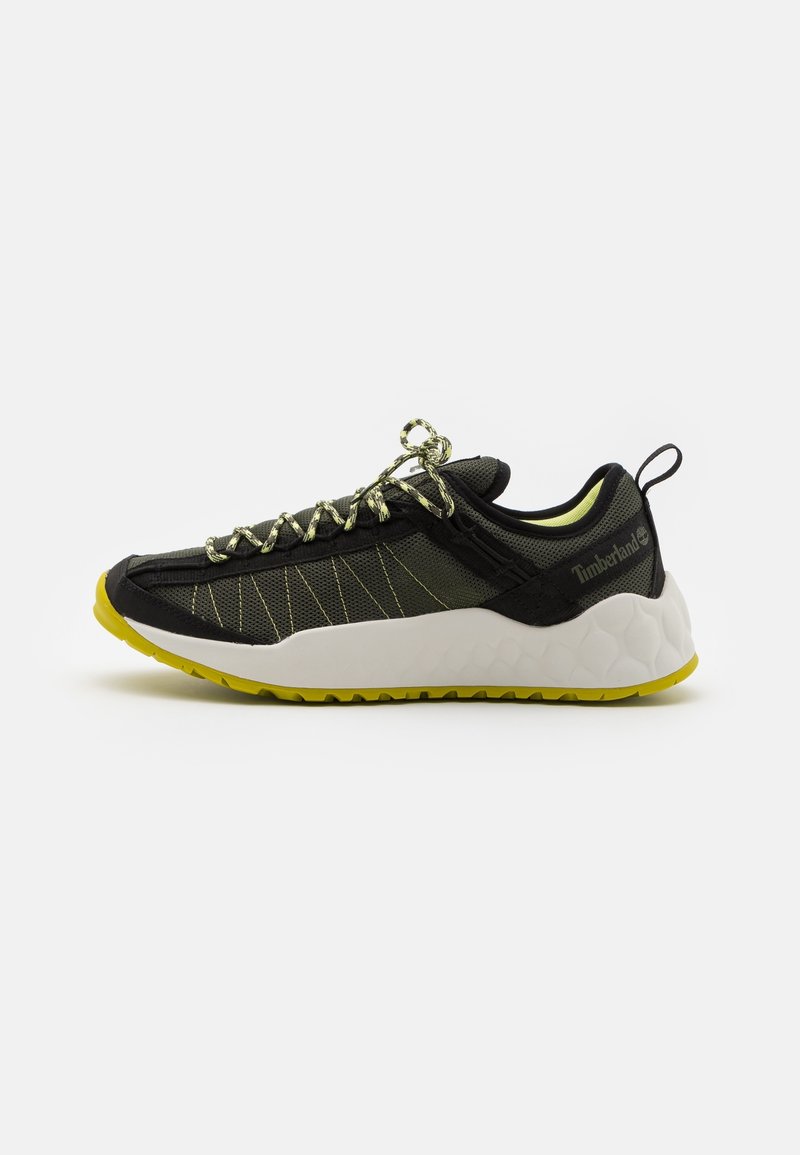 Baskets basses noires et vert olive avec une semelle intermédiaire blanche texturée nid d'abeille, une semelle extérieure jaune, des lacets à motifs et le logo Timberland sur le talon.