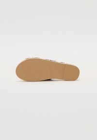 Sorte slip-on-sko med en teksturert overflate, med en beige gummisåle og subtilt mønster for bedre grep, som understreker holdbarhet og slitasjemotstand.