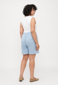 Shorts de algodón azul claro con una cinturilla elástica, combinados con una blusa sin mangas blanca. Los shorts tienen un ajuste relajado y son de longitud hasta la rodilla.