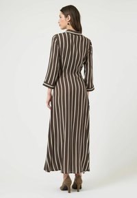 Robe maxi rayée marron et crème avec manches longues et taille cintrée, présentant une texture lisse et un ourlet évasé.