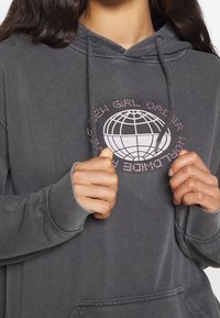 Grå hoodie med en grafisk design av en glob och text i rosa. Tillverkad av mjukt material med en avslappnad passform och känguruficka.