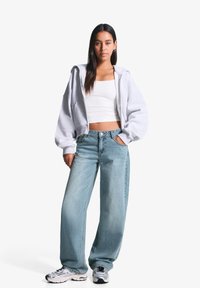 Hanorac supradimensionat gri, top alb scurt, blugi decoltați bleu deschis, și teniși argintii. Detalii notabile includ croiala lejeră și texturile moi.