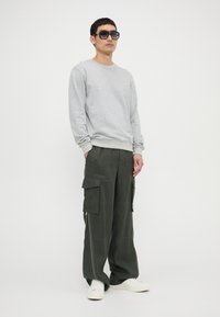 Gray sweatshirt with ribbed cuffs and hem, paired with loose, olive-green cargo pants featuring side pockets, complemented by white sneakers.
