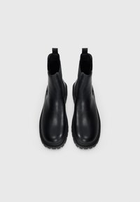 Botas negras de cuero hasta el tobillo con acabado suave, paneles laterales elásticos y suela de goma texturizada para mayor agarre. Cuenta con un lazo para facilitar su colocación.
