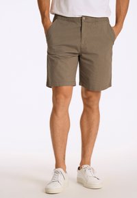 Pantaloni corti khaki con taglio dritto, chiusura a bottoni e tasche laterali. Realizzati in tessuto leggero con una finitura testurizzata. Indossati con sneakers bianche.