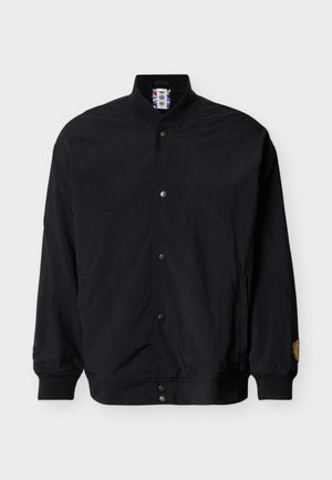 Črna bomber jakna s srajčnim gumbanjem, rebrastim ovratnikom, manšetami in spodnjim robom, z majhno nalepko na levi rokav in stranskimi žepi.