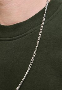 Sudadera verde de cuello redondo con cuello acanalado, combinada con un collar de cadena plateada brillante con eslabones entrelazados.