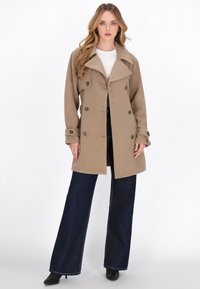 Beige wool blend coat with a double-breasted design, wide lapels, and button accents. Paired with high-waisted dark denim pants.