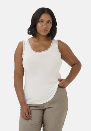 Weißes, geripptes Tanktop mit Spitzenverzierung am Halsausschnitt und den Schultern, verfügt über ein figurbetontes Design und eine weiche Textur. Kombiniert mit beigen Hosen.