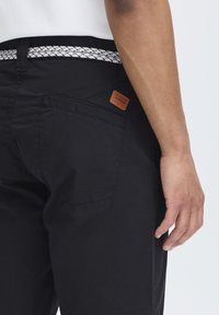 Pantalons noirs en tissu texturé. Présentent une étiquette en cuir sur la poche arrière et une ceinture à motifs. Coupe ajustée et design à jambe droite.