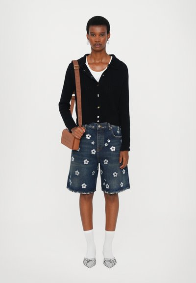 Cardigan negru cu striții, tricou alb, pantaloni scurți din denim cu broderie florală, sosete albe și pantofi cu model. Geantă maro cu text embosat.