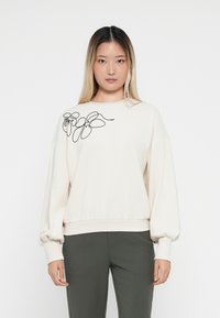 Lichtbeige sweatshirt met zwarte bloemenborduursel op de linker schouder, met lange, volumineuze mouwen en een ribgebreide zoom.