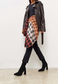 Brown leather jacket, black fitted top, plaid wrap skirt with red, yellow, and blue checks, paired with black ankle boots and dark trousers.