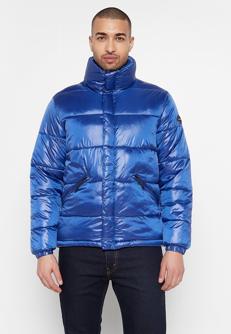 Blaues Puffer-Jackett aus glänzendem Material, mit hohem Kragen, horizontal gestepptem Design und zwei schwarzen Reißverschlusstaschen.