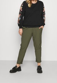 Czarna bluza z haftem kwiatowym na rękawach, w połączeniu z oliwkowymi spodniami i czarnymi butami na grubej podeszwie. Casualowy fason.