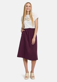 Haut à manches courtes blanc avec un motif floral, associé à une jupe mi-longue élastique taille haute de couleur violet profond. Des chaussures à plateforme beiges complètent le look.