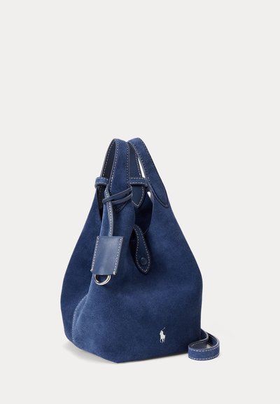 Blå mokkasinputsväska med läderdetaljer, dragsko och justerbar rem. Har en liten etikett med metallbeslag.