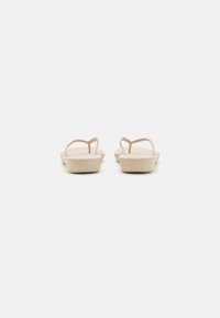 Flate sandaler i beige med minimalistisk design, tynne stropper og en glatt, teksturert såle. Enkel og elegant silhuett.