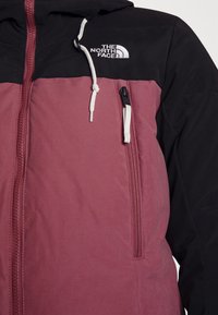 Dwukolorowa kurtka na zamek w odcieniach bordo i czerni z białym logo The North Face oraz przednią kieszenią na zamek z białym suwakiem na klatce piersiowej.