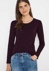 Langærmet, rundhalset bluse i mørk lilla stof, parret med lyseblå jeans med dobbeltknaplukning og sidelem.