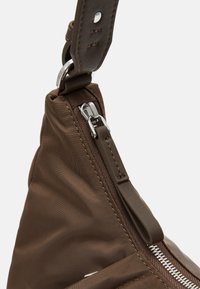 Sac à épaule en nylon marron avec fermeture éclair et bandoulière en cuir. Agrémenté d'un quincaillerie en acier inoxydable et d'une surface en tissu texturé.