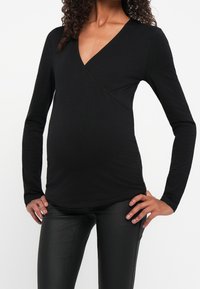 Top negro de manga larga envolvente, hecho de una tela suave, con un escote en V profundo y un diseño ajustado, combinado con leggings negros con aspecto de cuero.