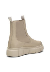 Botín de piel beige hasta el tobillo con paneles laterales elásticos y tiradores. Suela blanca gruesa con textura estriada. Superficie superior suave, con un mínimo de detalles.