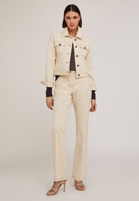 Jachetă din denim bej cu două buzunare pe piept și închidere cu nasturi, asortată cu pantaloni cu talie înaltă. Textură ușoară, croială dreaptă și detalii minime.
