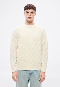 Kötött krémszínű pulóver kerek nyakkivágással, bordázott passzékkal az ujjakon és az alján. Világoskék farmer fölött viselve. Puha anyagú és laza szabású.