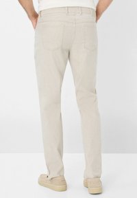 Light beige cotton blend trousers with a straight cut, back pockets, and subtle texture. Paired with light-colored slip-on shoes.