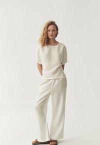 Linen top with short, puffed sleeves, paired with loose, lightweight white pants and flat sandals. Textured beige fabric, minimal design.