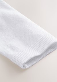 Witte geribde stoffen mouw met elastische boord, met zichtbare gebreide textuur en een gevouwen einde op een neutrale achtergrond.