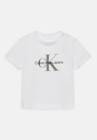Camiseta blanca de algodón con un gran logo "CK" en gris y el texto "Calvin Klein Jeans" en negro. Mangas cortas con cierre de broche en el hombro.