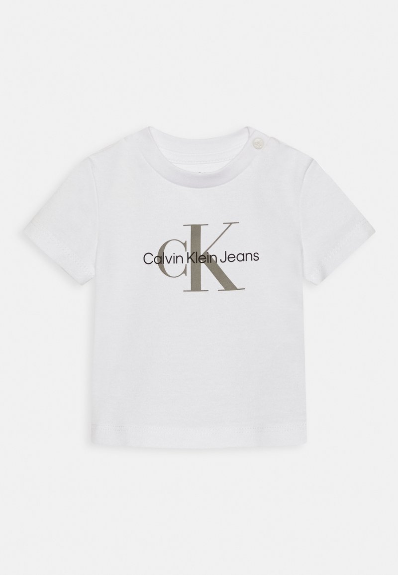 Camiseta blanca de algodón con un gran logo "CK" en gris y el texto "Calvin Klein Jeans" en negro. Mangas cortas con cierre de broche en el hombro.