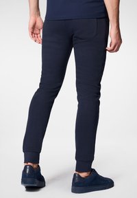 Granatowe spodnie dresowe z prążkowanymi mankietami, posiadające dopasowany krój i kieszenie z tyłu. Noszone z dopasowanymi granatowymi sneakersami.