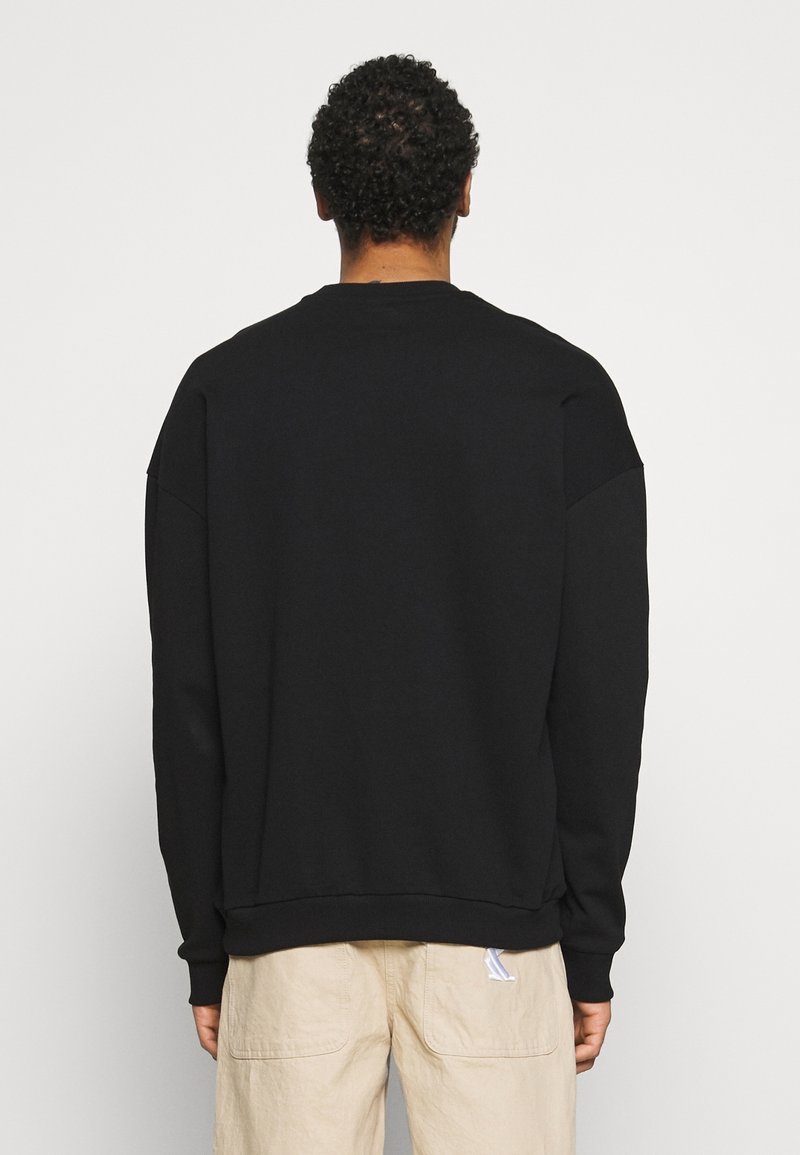 Sweatshirt noir en tissu doux, avec un col rond classique, des coutures d'épaule tombantes et un ourlet à côtes. Design simple et minimal.